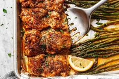 chicken and asparagus in a baking pan with lemon wedges on the side