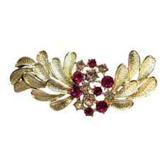 a gold and red broochle with leaves on it's side, set against a white background