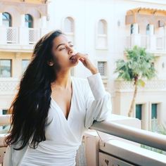 a woman standing on a balcony with her hand in her mouth and looking up at the sky