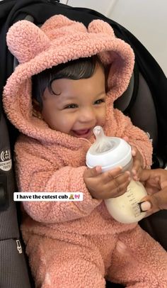 a baby in a pink teddy bear outfit sitting in a stroller and holding a bottle