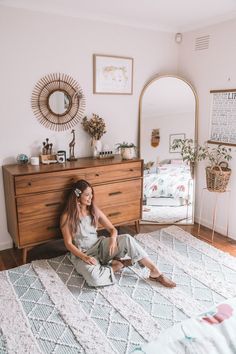 a woman sitting on the floor in front of a dresser