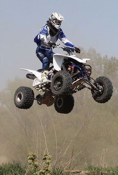 a man riding on the back of a white four - wheeler through the air in front of trees