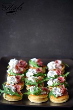 small appetizers are arranged on a black plate with green garnishes