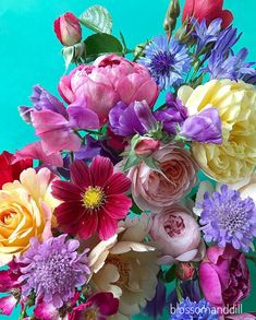 a vase filled with lots of colorful flowers on top of a blue table next to a wall