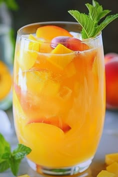 a glass filled with fruit and garnish on top of a table next to sliced peaches