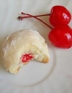 two cherries sitting on top of a white plate next to a donut hole