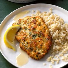 a white plate topped with chicken and rice next to a lemon wedge on a green table