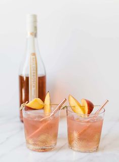 two glasses filled with apple cider cocktails next to a bottle on a marble counter