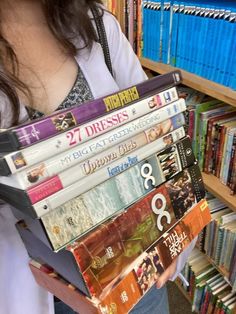 a woman holding a stack of dvd's in front of a bookshelf