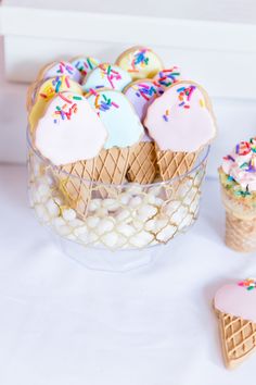 some ice cream cones and cookies are in a glass bowl on a white tablecloth