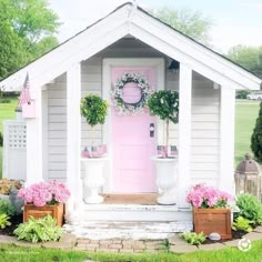 a white house with pink front door and potted plants on the porch, in front of it