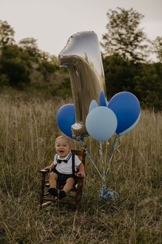 a baby sitting in a chair with blue and silver balloons attached to it's back