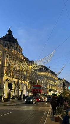 people are walking down the street in front of buildings with christmas lights strung across them