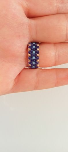 a person's hand holding a ring with blue and yellow beads on it,