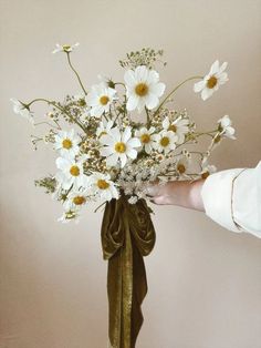 a bouquet of daisies and other flowers in a vase held by a person's hand