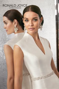 two beautiful women in white dresses standing next to each other and one is looking at the camera