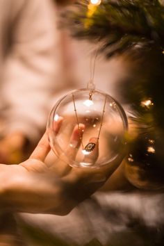 a person holding a glass ornament in front of a christmas tree with lights