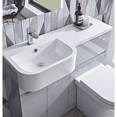 a white toilet sitting next to a sink in a bathroom under a mirror and tiled walls