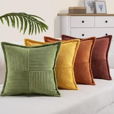 four different colored pillows sitting on top of a white couch next to a potted plant