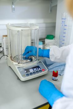 a person in white lab coat and blue gloves working on a machine