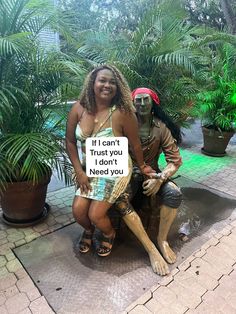 two people sitting on a statue with a sign that says i can't trust you, i don't need you