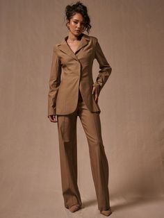 a woman standing in front of a white backdrop wearing a tan suit and brown shoes