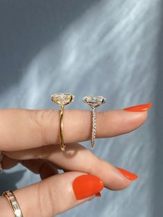 a woman's hand with two rings on it and an orange manicured nail