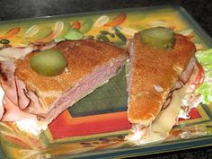 a sandwich with meat, cheese and pickles on it sitting on a colorful plate