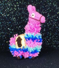 a pink and blue llama stuffed animal sitting on top of a pile of confetti