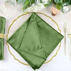 a place setting with green napkins and gold rimmed utensils on a white table cloth