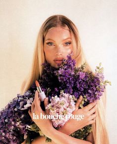 a woman with long blonde hair holding flowers and lipstick