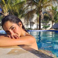 a woman in a swimming pool with palm trees behind her and the water is blue