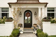 a white house with lots of plants and pumpkins on the front door, along with potted trees