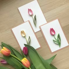 three cards with tulips on them sitting on a table next to some flowers