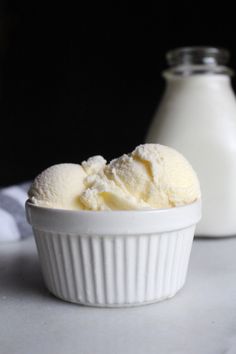 two scoops of ice cream in a white bowl next to a bottle of milk