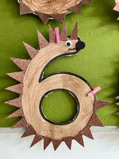 the number six is made out of wood and has pink spikes on it's head