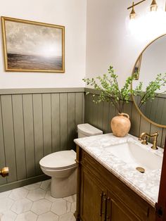 a white toilet sitting next to a sink in a bathroom under a framed painting on the wall