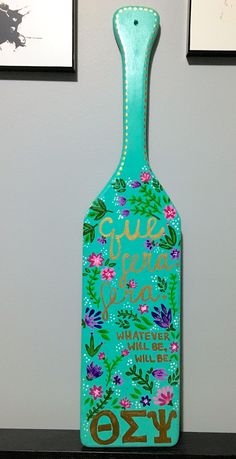 a green bottle with flowers painted on it sitting on a shelf next to two framed pictures