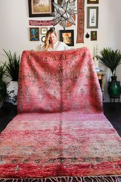 a woman sitting on top of a couch covered in a red blanket next to pictures