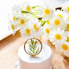 a wedding ring sits on top of a small white cake with daisies in the background