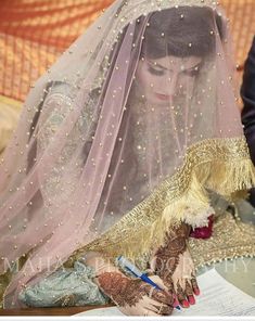 a woman in a veil writing on a piece of paper while wearing a wedding dress