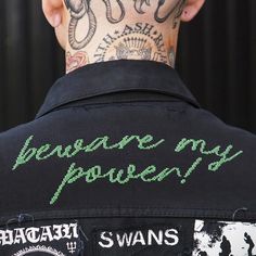 a tattooed man wearing a black jacket with green writing on it