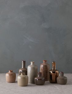 there are many vases lined up on the table with grey walls in the background