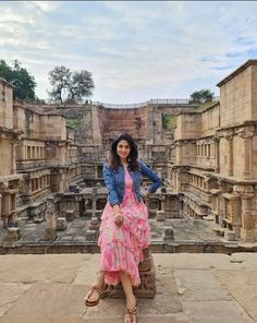 a woman in a pink dress is posing for a photo at the ruins of an ancient city