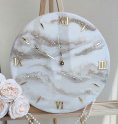 a marble clock sitting on top of a wooden shelf next to flowers and pearls hanging from it's sides