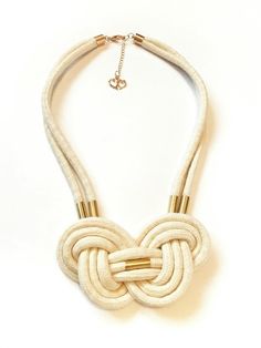 a white and gold necklace with an intricate knot design on it's neckline