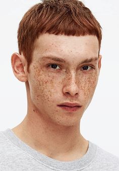 a young man with freckles on his face looks at the camera while wearing a grey shirt