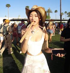 a woman in a white dress and straw hat holding a long stick at an outdoor event