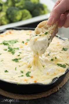 a person dipping cheese into a skillet with broccoli in the background