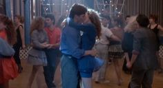 a man and woman kissing on the dance floor in front of a group of people